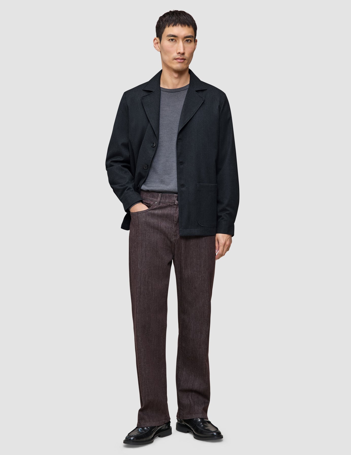 Ein Mann, der ein Atelier Overshirt Dark Navy über einem grauen T-Shirt, eine braune Atelier-Hose und schwarze Lederschuhe trägt.